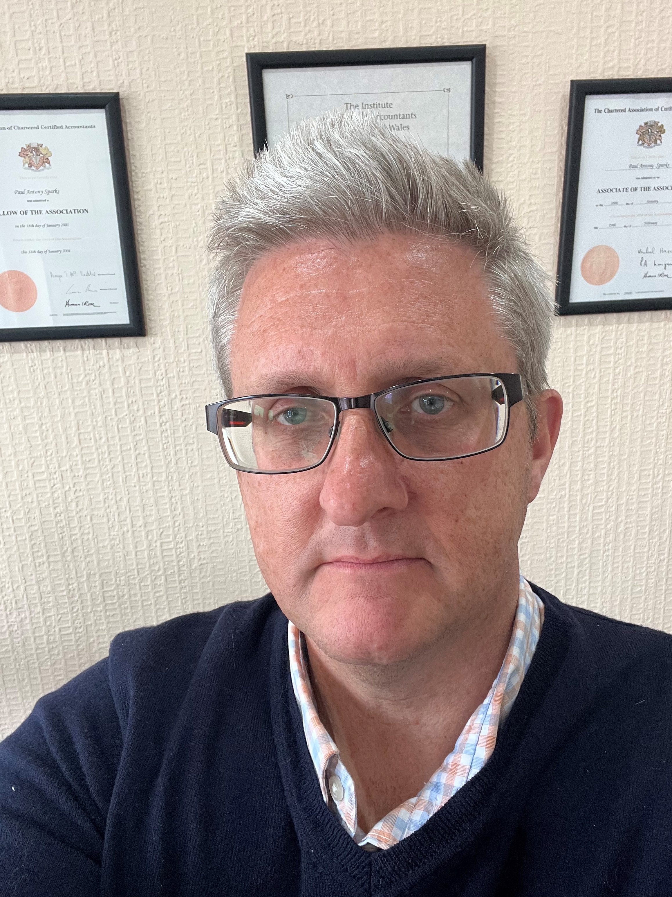 Profile picture of Paul Sparks. A white man with short silver hair and glasses. Behind him are framed certificates.